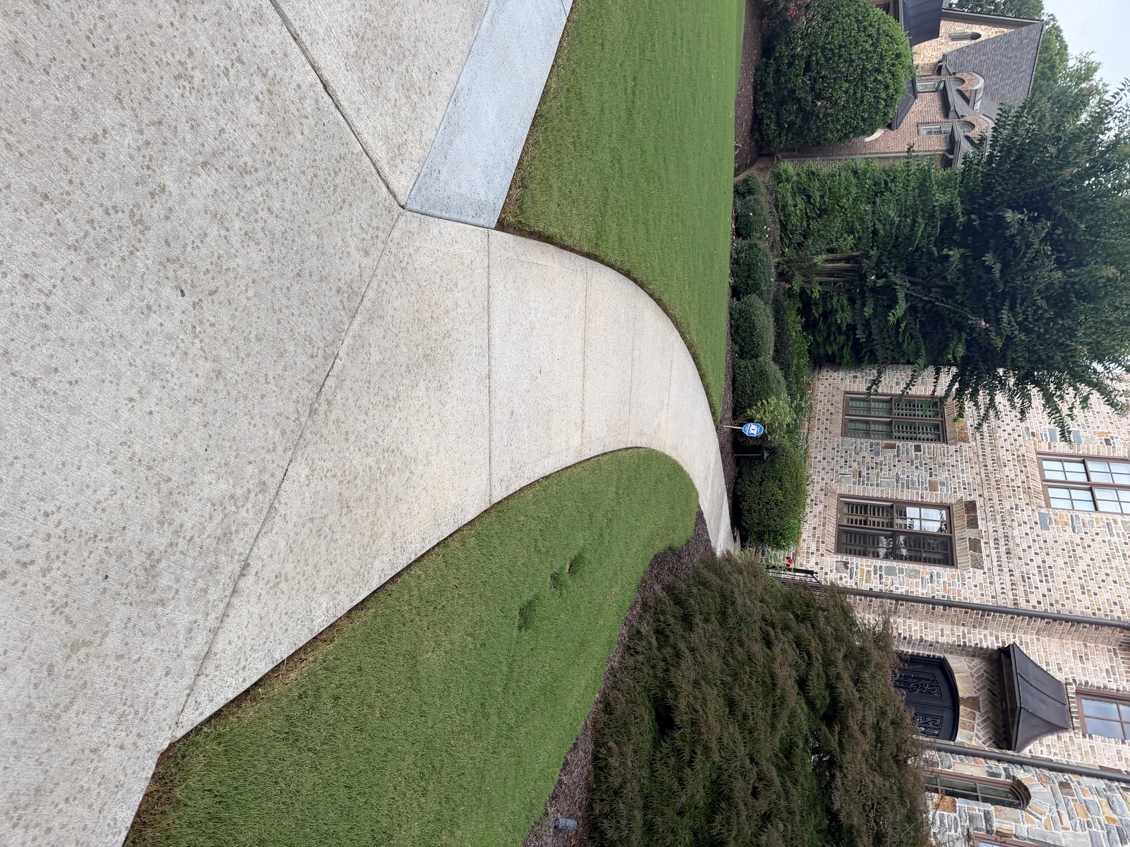A freshly pressure-washed concrete driveway sweeping up to a stone home by KM Property Restorations in metro Atlanta