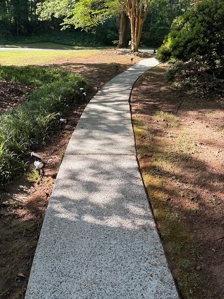 A long concrete walkway pressure-washed clean through a wooded yard by KM Property Restorations